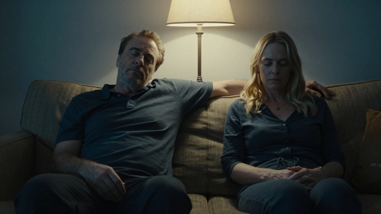 Two people sit silently on a couch after intimacy, bathed in soft lamplight.